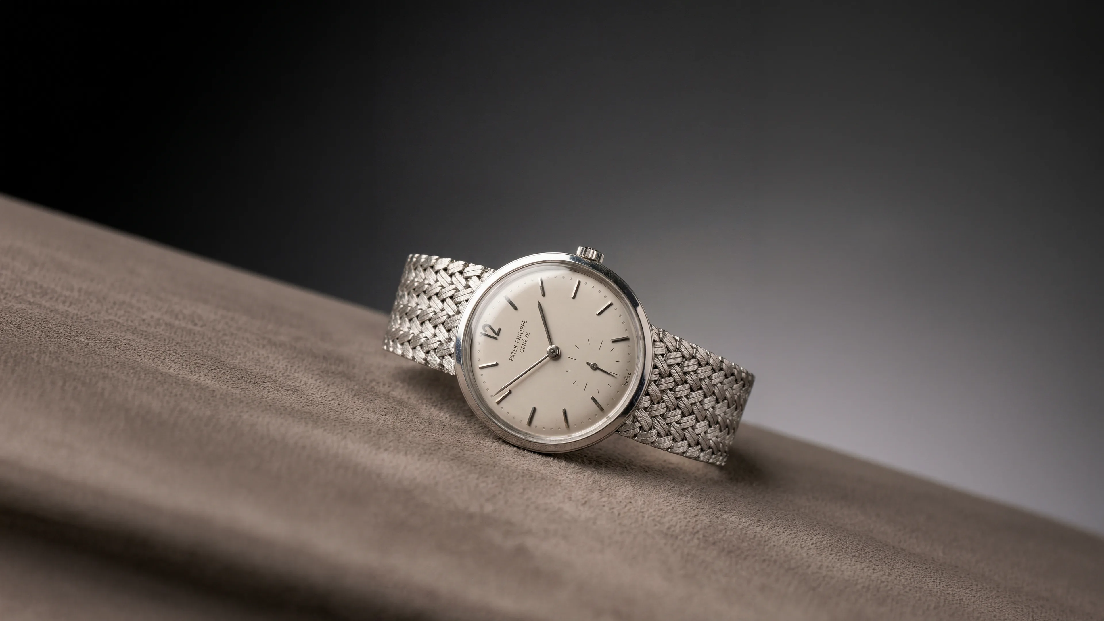 A Patek Philippe dress watch on a woven bracelet, resting on suede